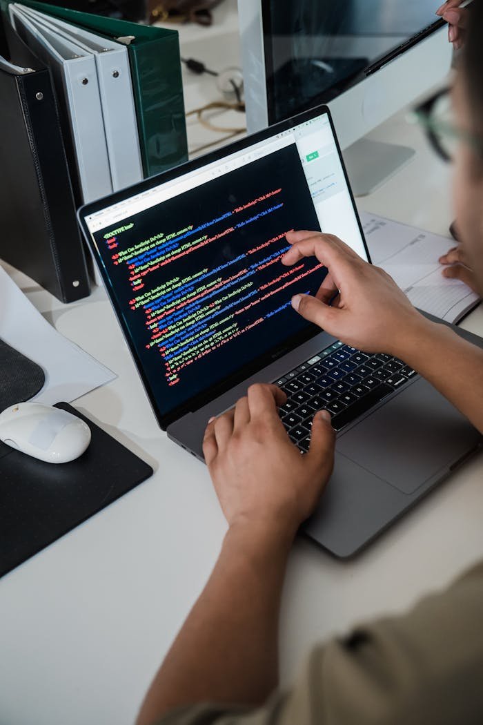 Leistungen Close-up of a programmer pointing at a colorful code script on a laptop in an office setting.