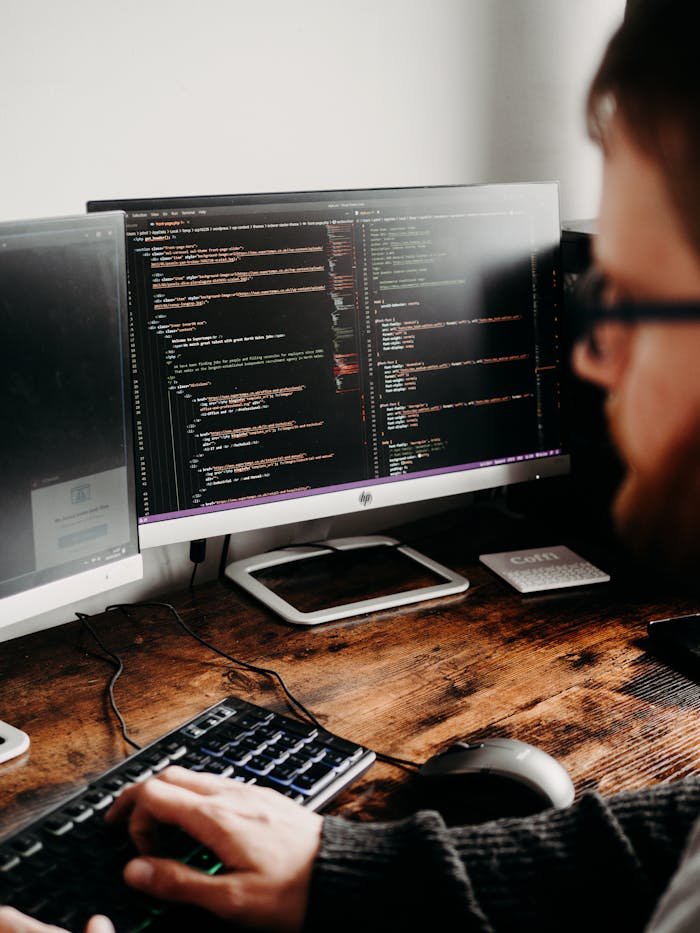 Leistungen Focused software developer at desk coding with multiple monitors in a modern workspace.