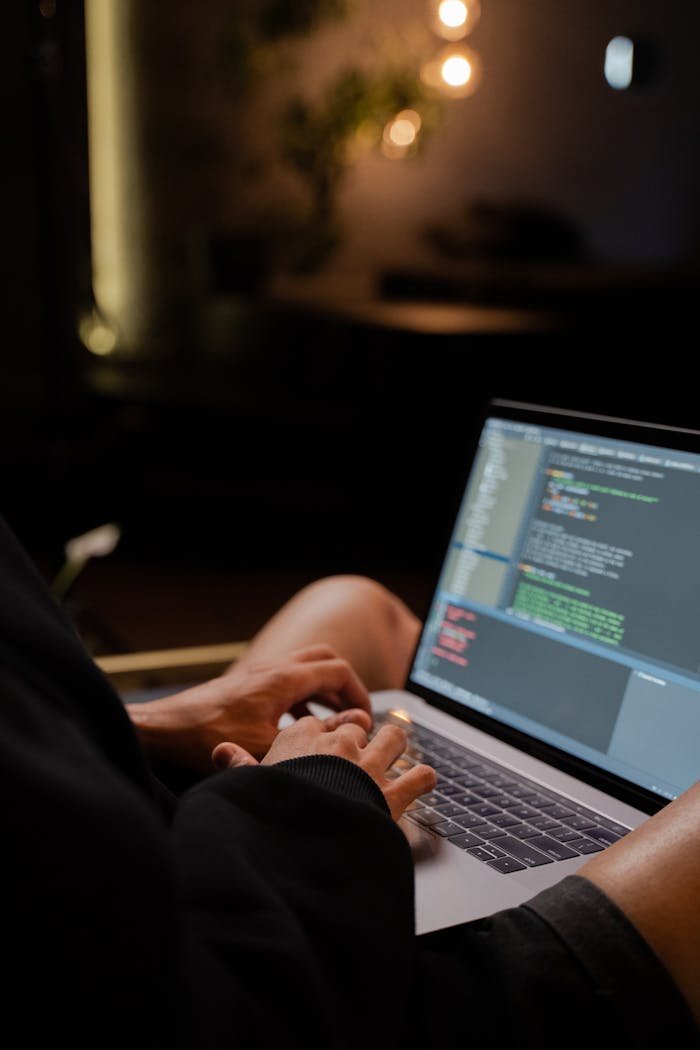 Über uns Focused hands typing code on a laptop in a dimly lit room, showcasing programming activities.